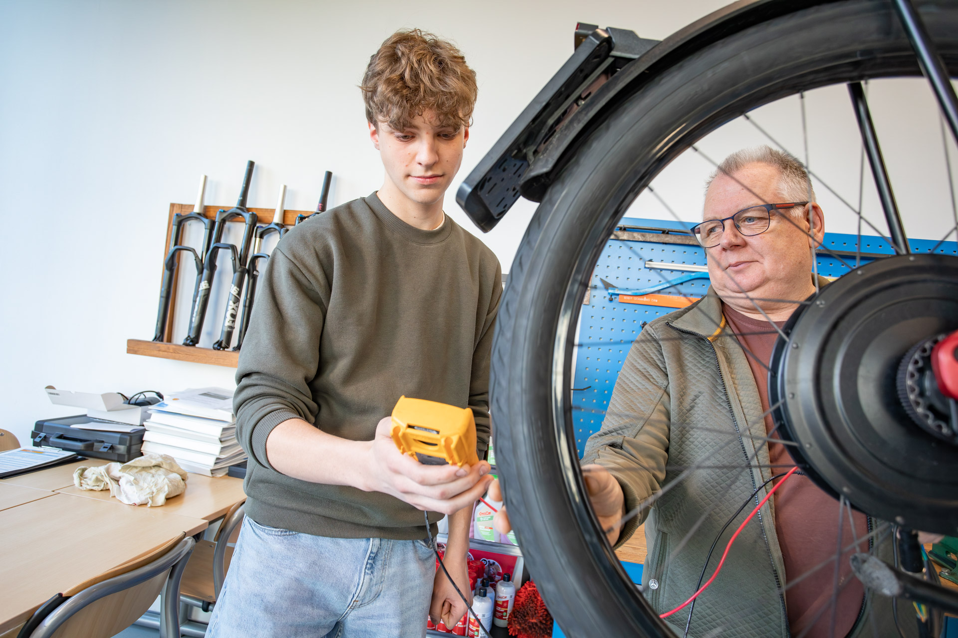 Een man en jongen kijken naar een meetapparaat terwijl je op de voorgrond een wiel van een fiets ziet