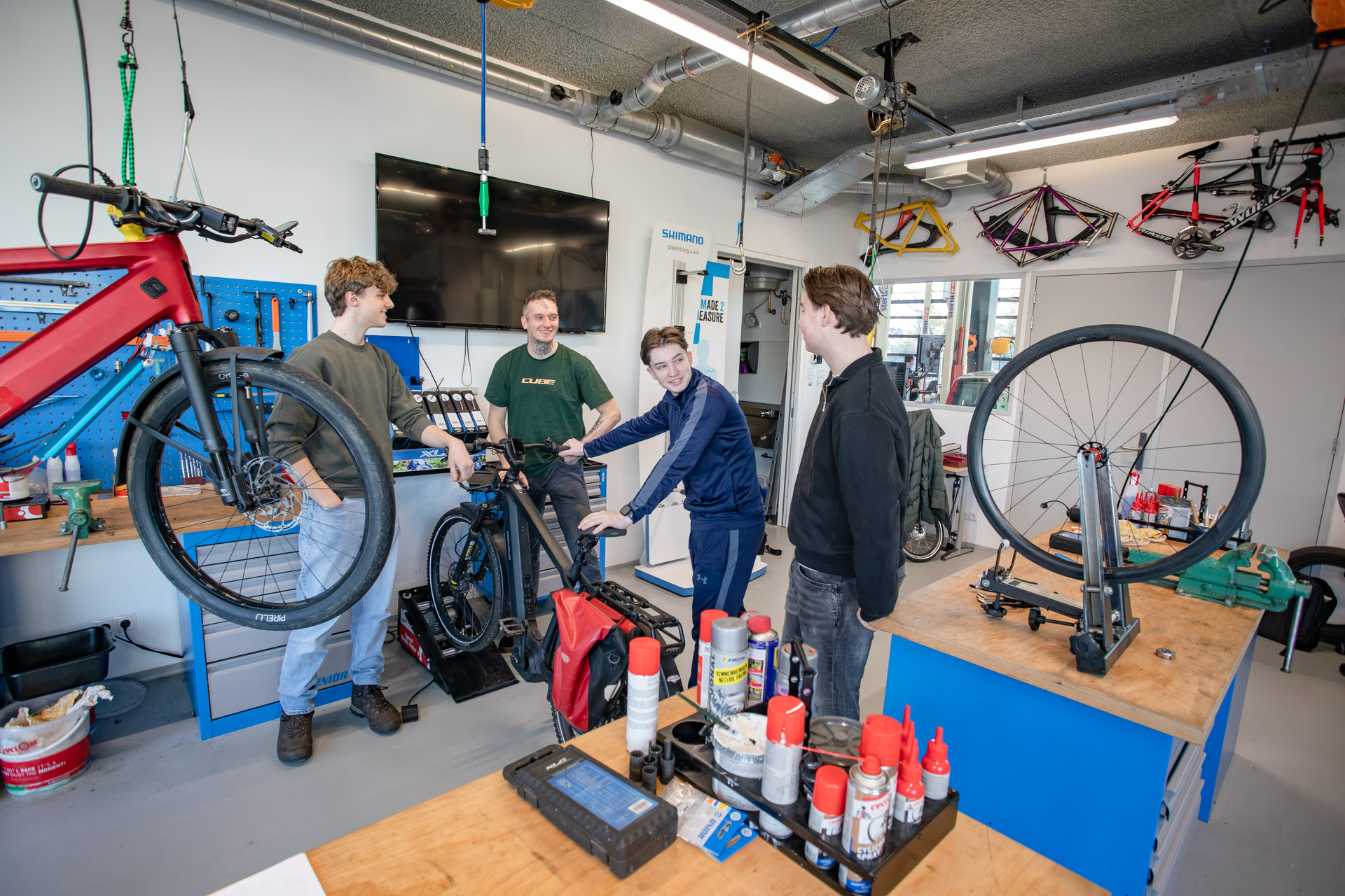 Vier jongens in een fietsenwerkplaats staan om een fiets heen te praten.