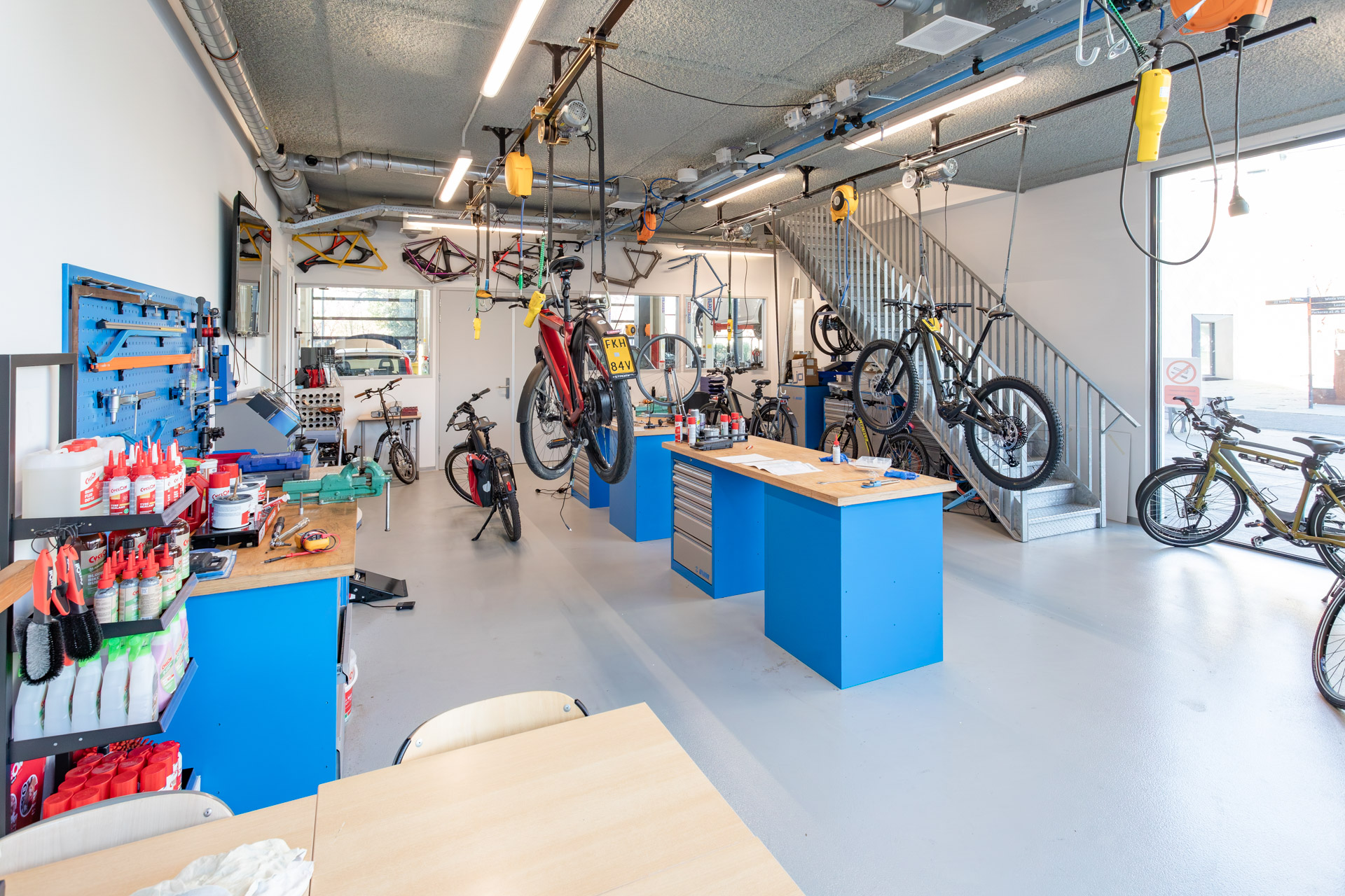 Je ziet een werkplaats waar fietsen staan en aan het plafond hangen