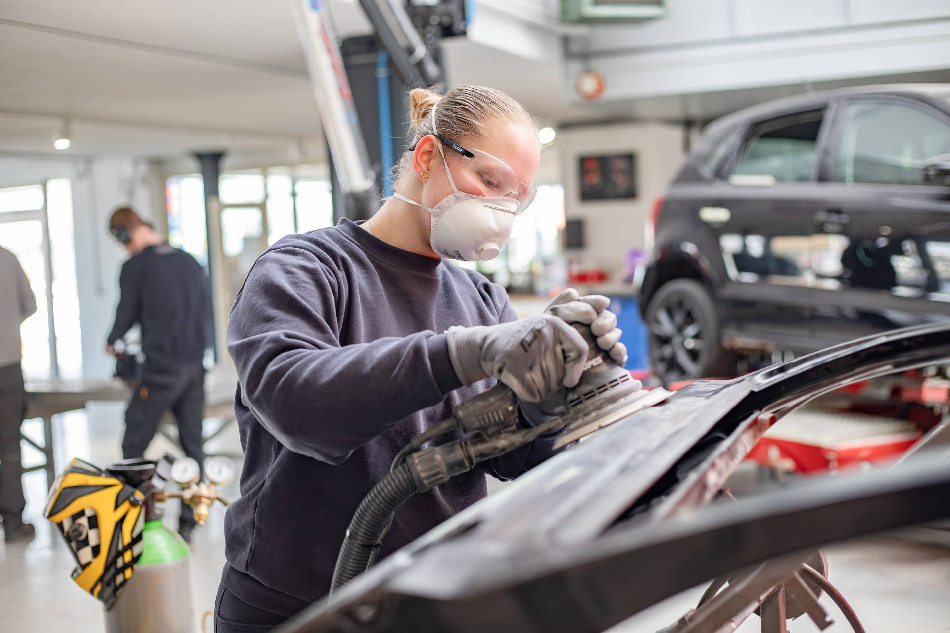Een meisje met masker en beschermingsbril op dat aan het schuren is in een garage.