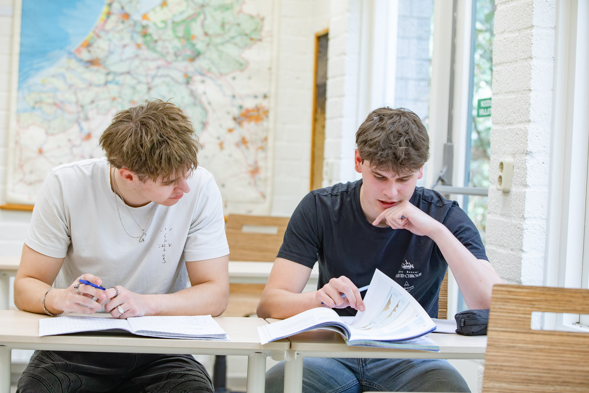 Twee jongens in een klaslokaal overleggen en werken in hun schrift.