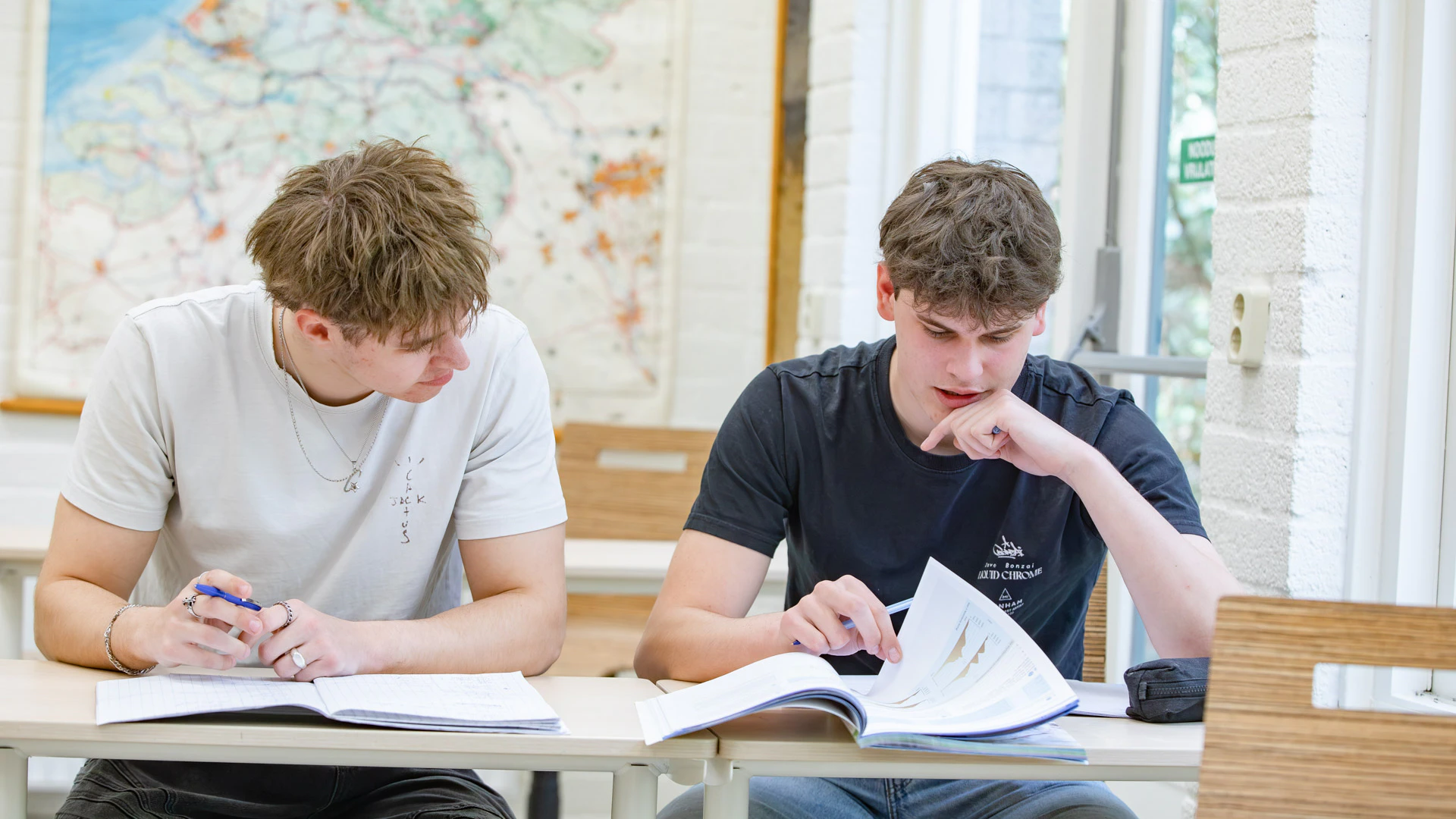 Twee jongens in een klaslokaal overleggen en werken in hun schrift.