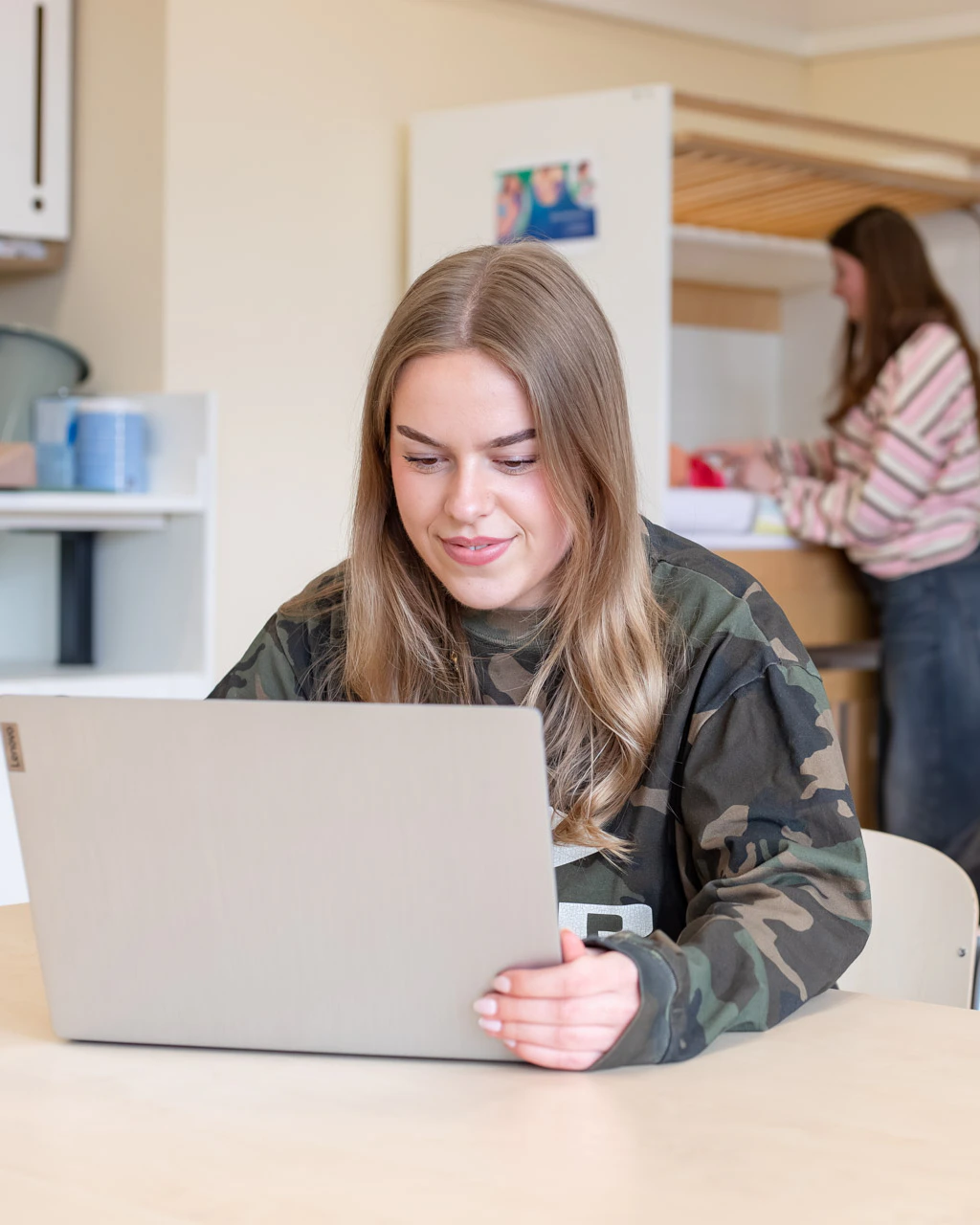 Meisje zit in een klaslokaal en werkt achter haar laptop.