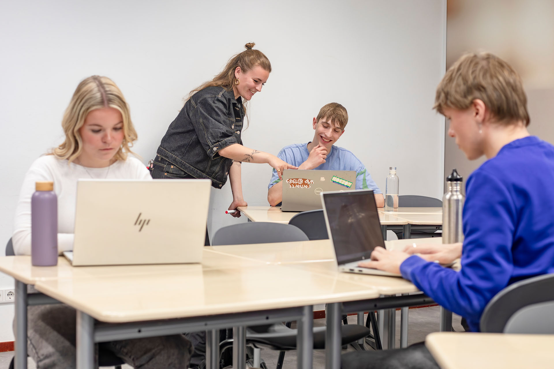 Een jongen in een klaslokaal krijgt uitleg van een docent bij zijn laptop.