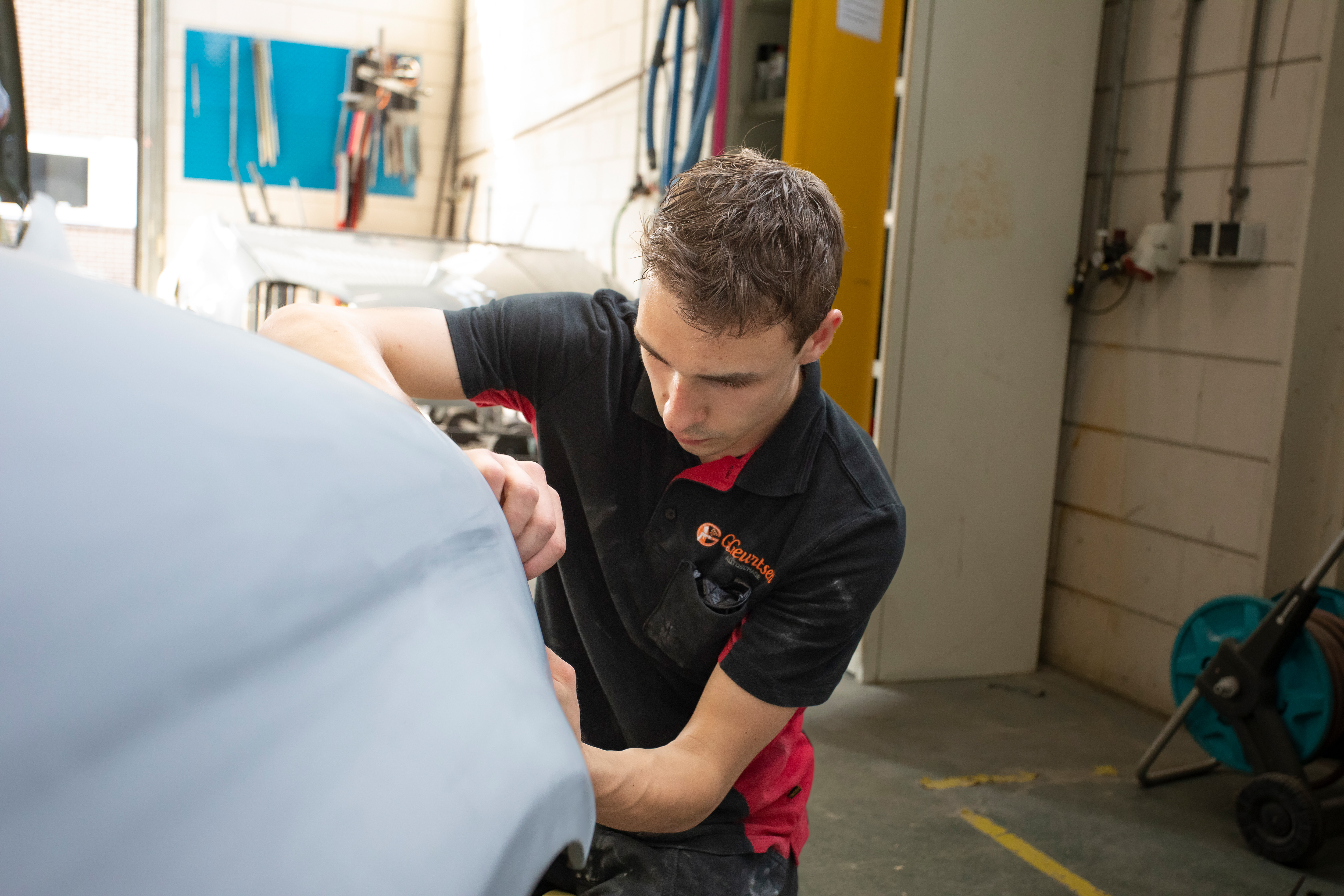 Jongen in werkkleding is bezig met de voorkant van een auto te plakken