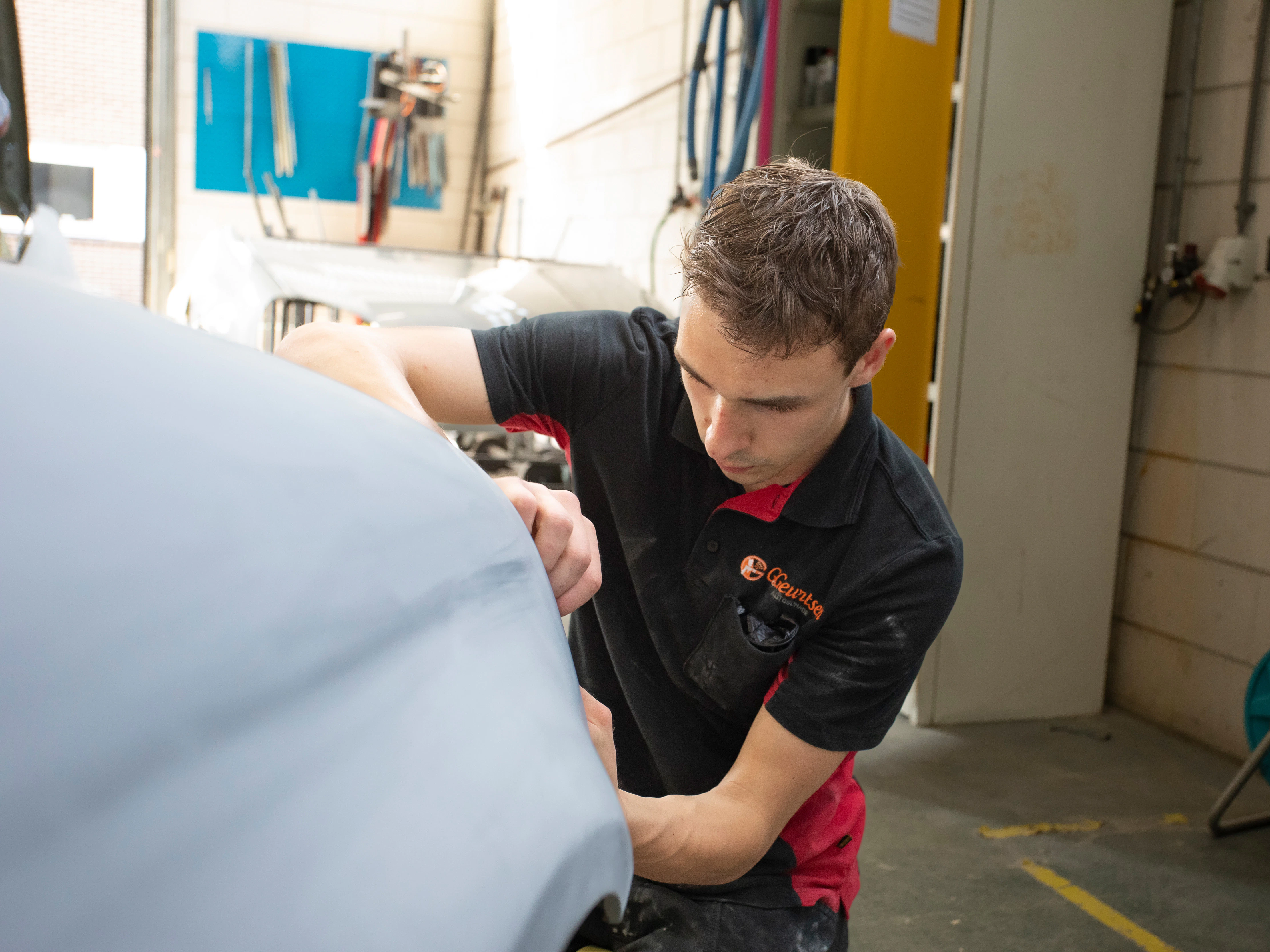 Jongen in werkkleding is bezig met de voorkant van een auto te plakken