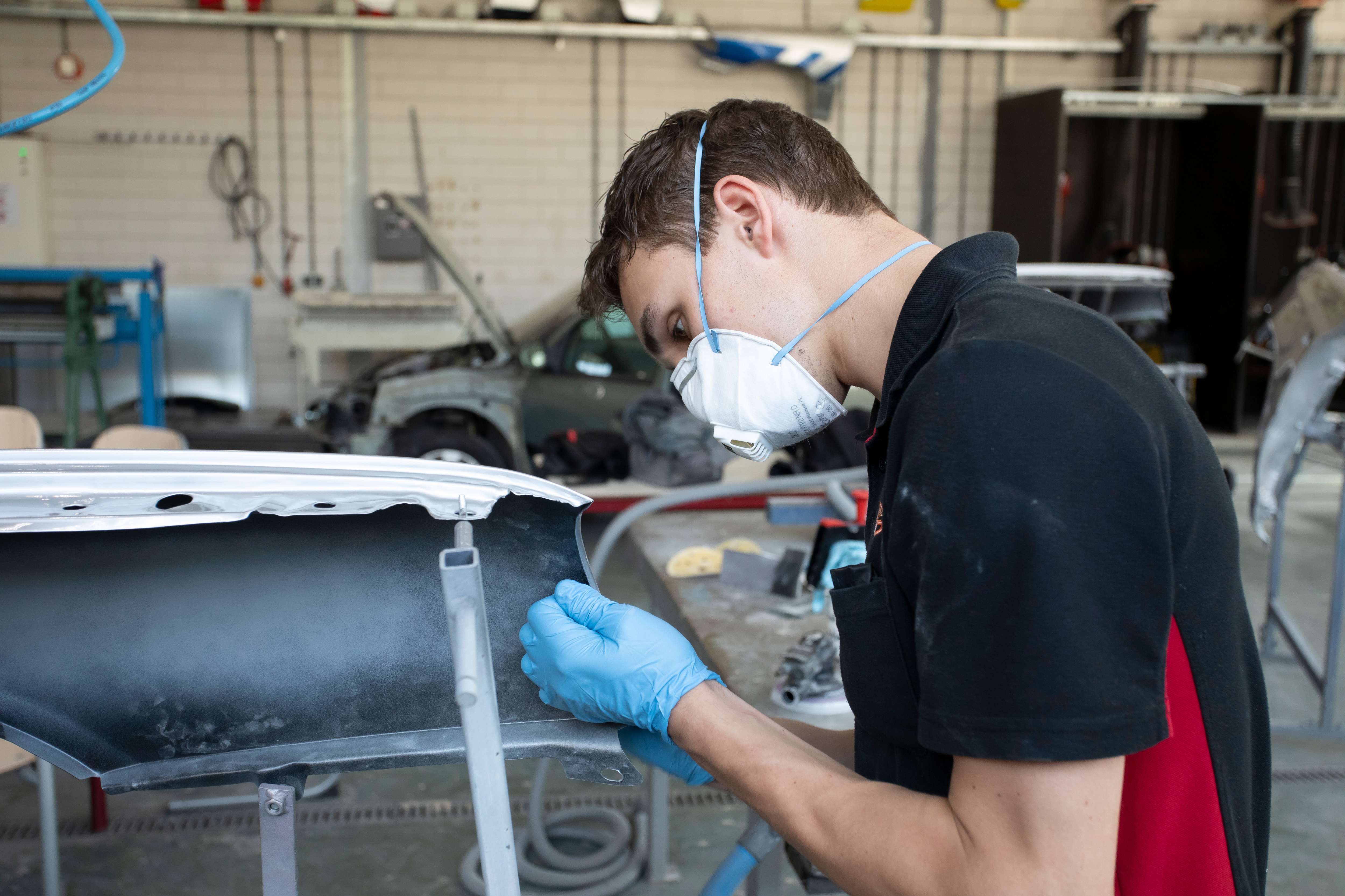 Student met een mondkapje op is bezig met autoschade herstellen