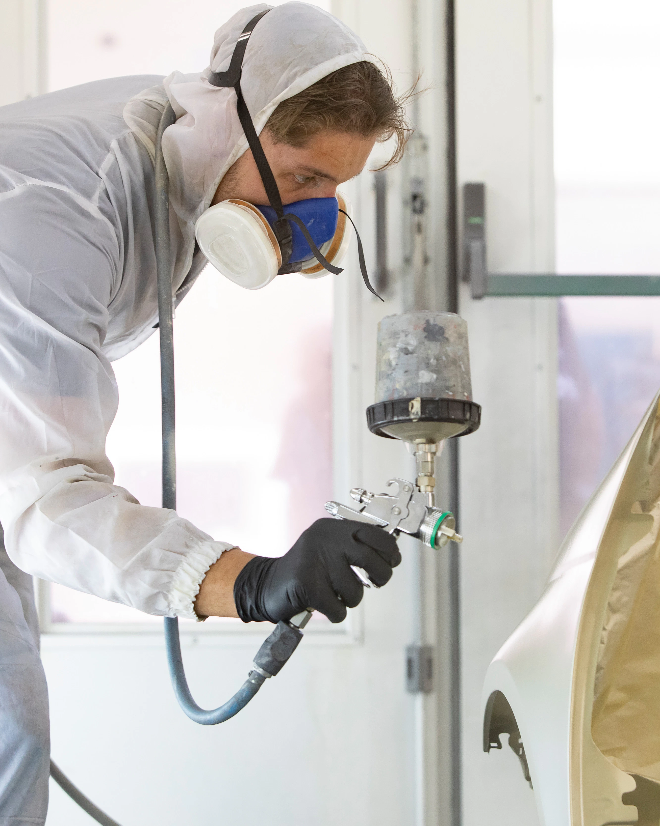 Jongen in een wit pak heeft een apparaat in de hand waarmee hij iets aan het spuiten is met een gouden kleur