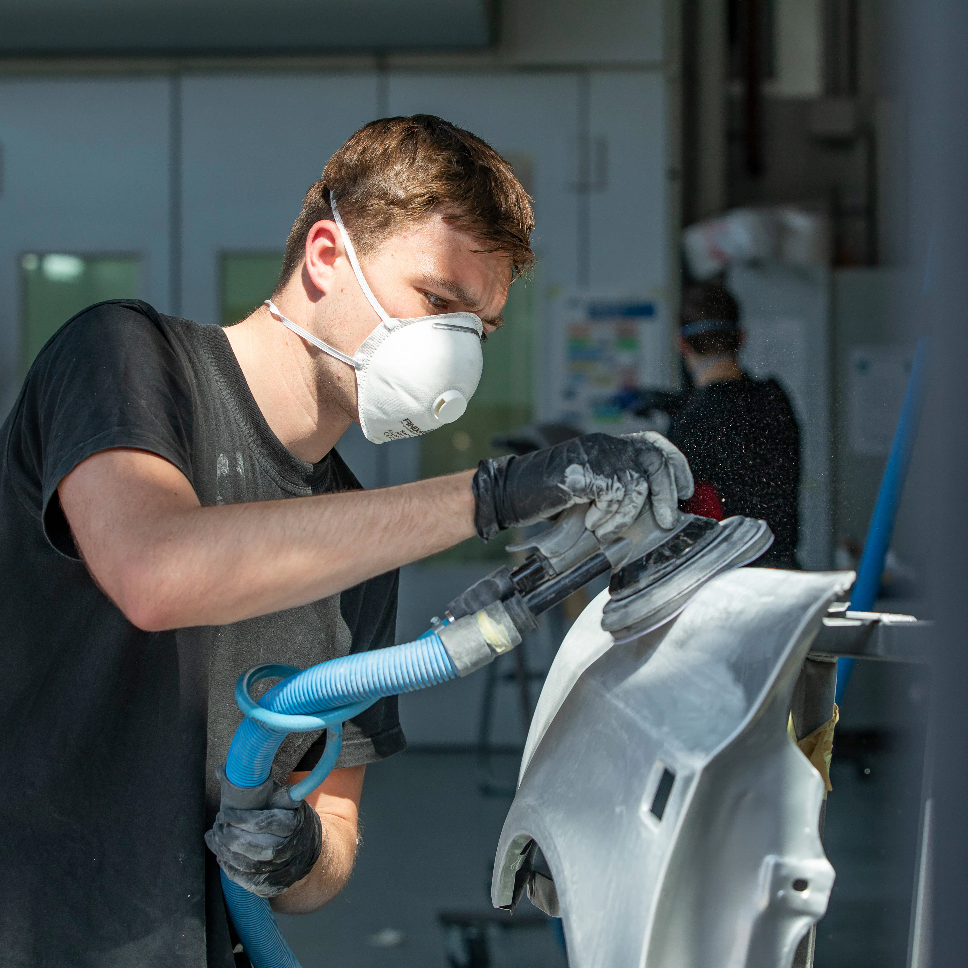 Jongen met een mondkapje op heeft een apparaat in de hand waarmee hij een onderdeel van de auto aan het schuren is