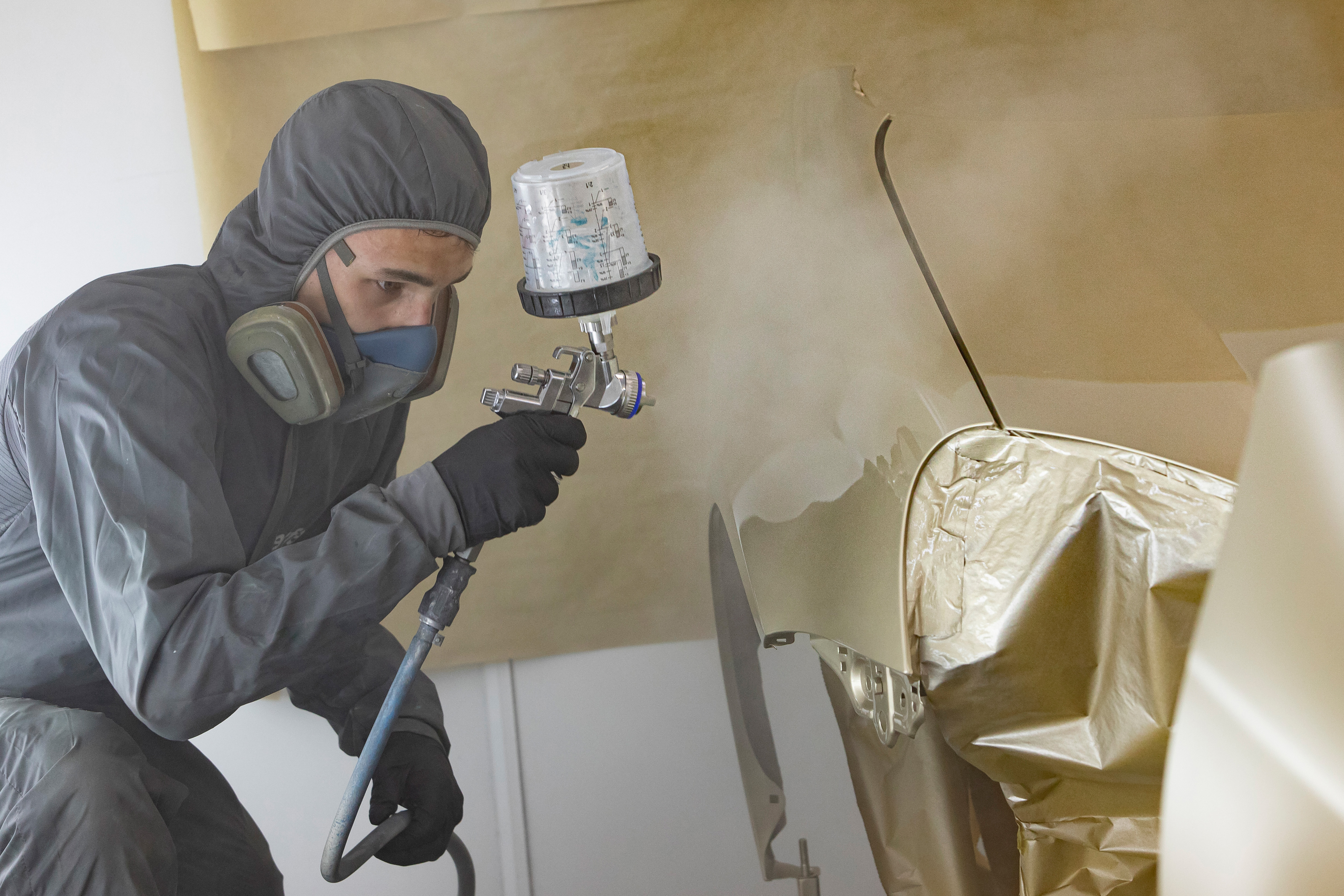 Jongen in een zwart pak is een onderdeel van de auto aan het spuiten met een gouden kleur