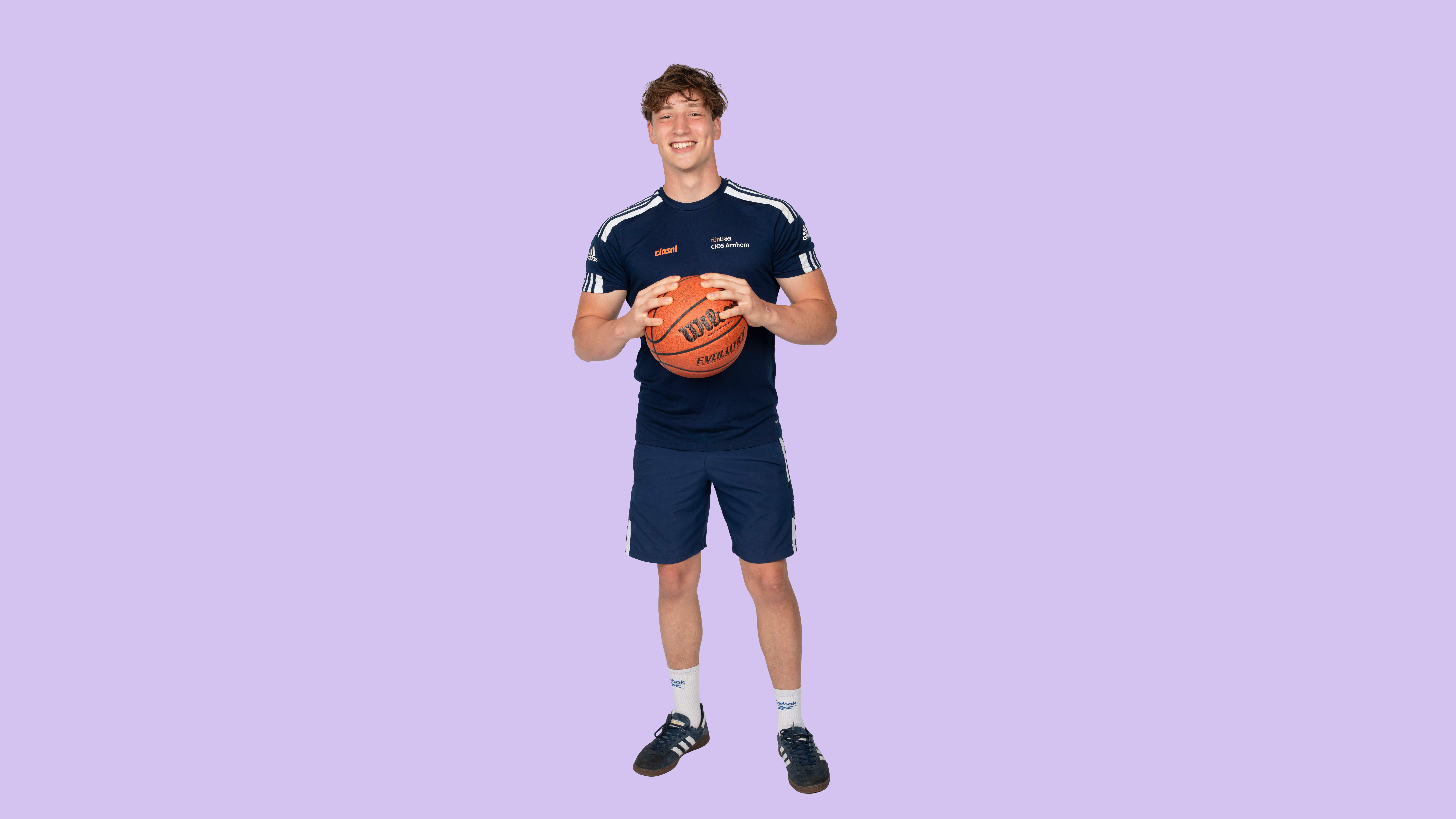 Jongen in sportkleding houdt een basketball vast en kijkt in de camera