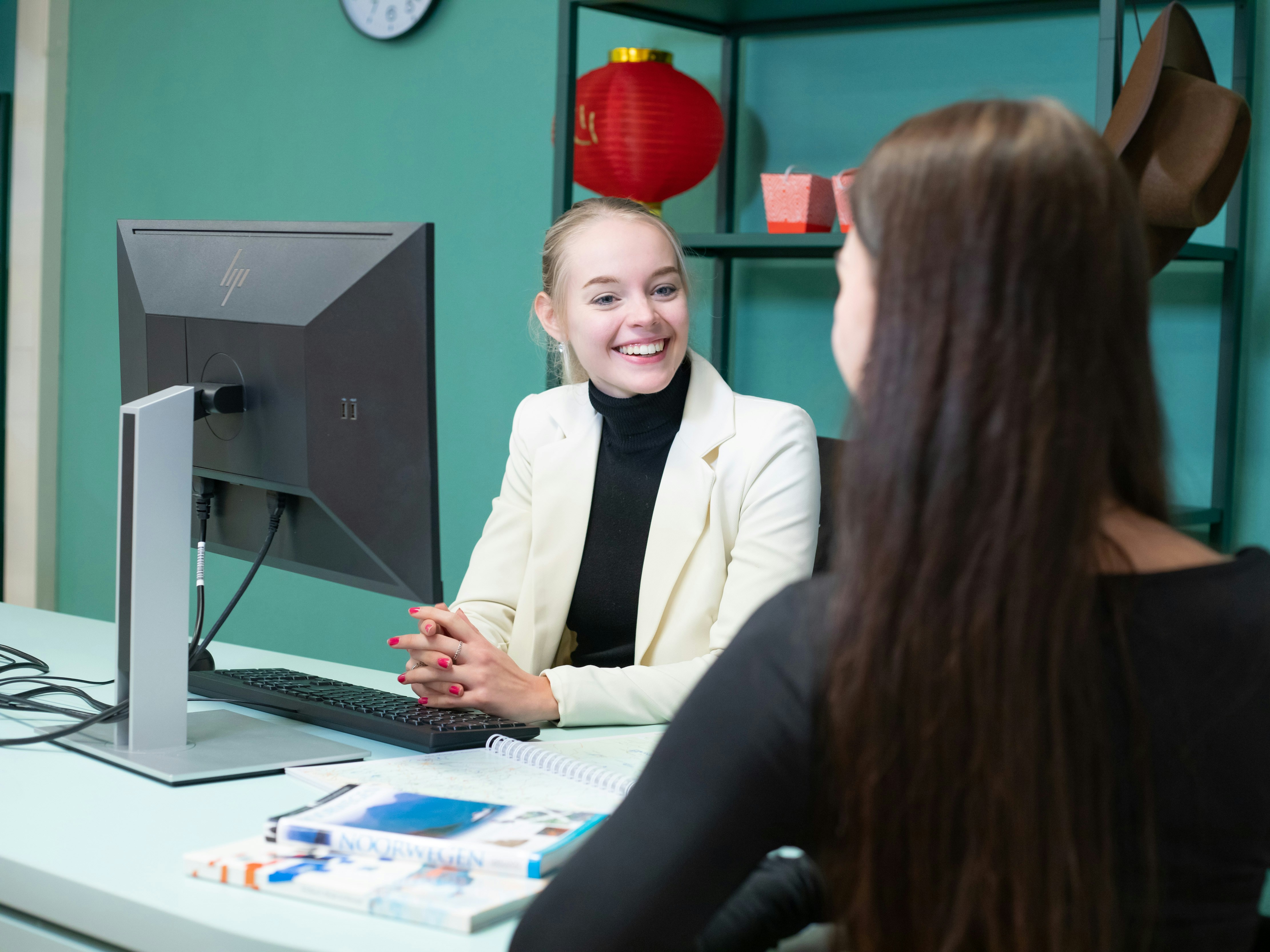 Student zit achter een computer en er ligt een reisboek op tafel