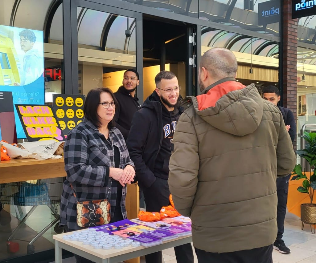 Jongerenwerkers en docenten geven uitleg aan een voorbijganger in een winkelcentrum.