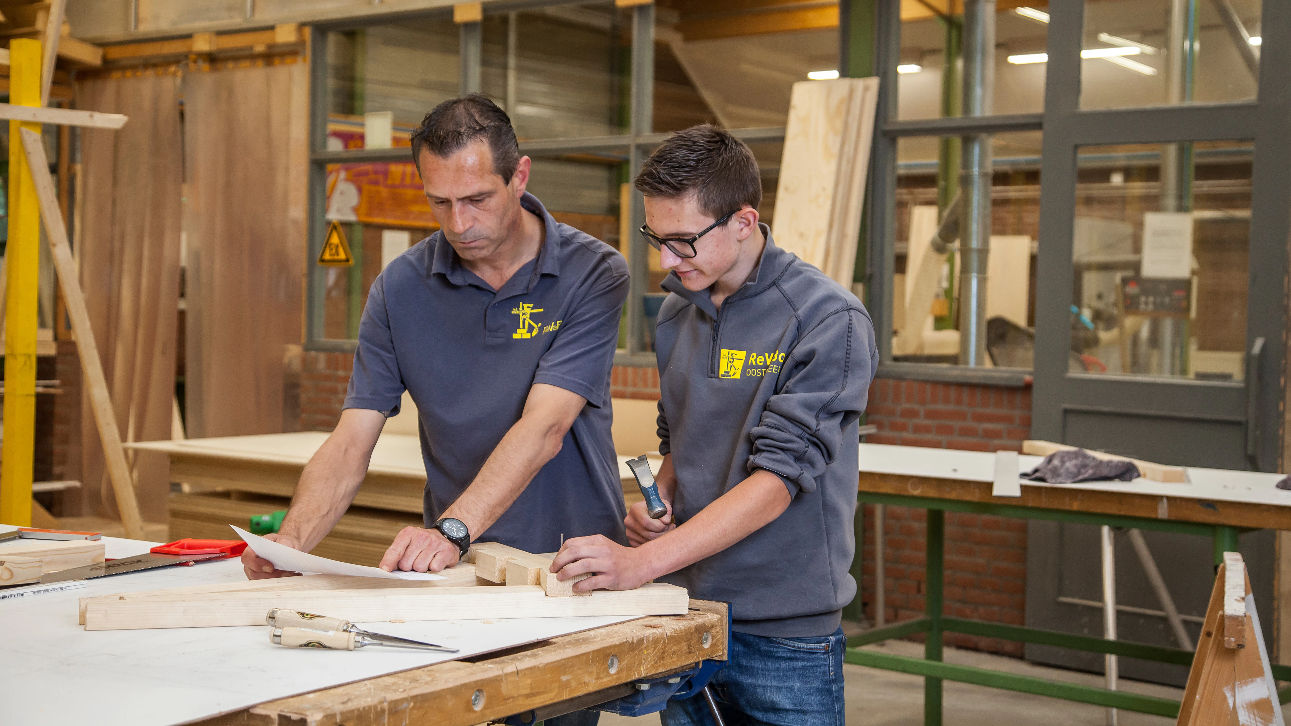 Jongen is iets aan het opmeten om te timmeren samen met de docent