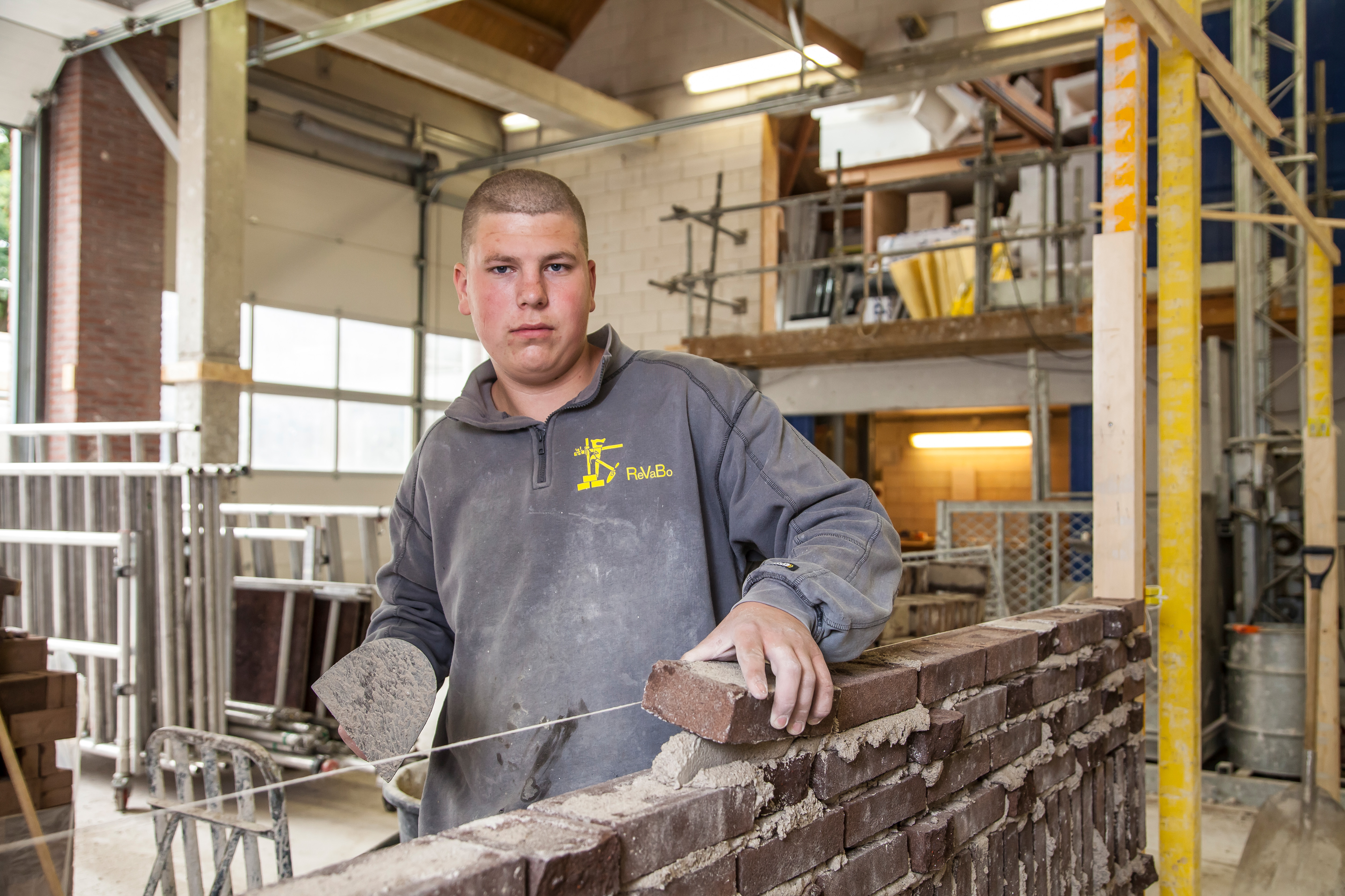 Jongen kijkt naar camera terwijl hij muurtje metselt
