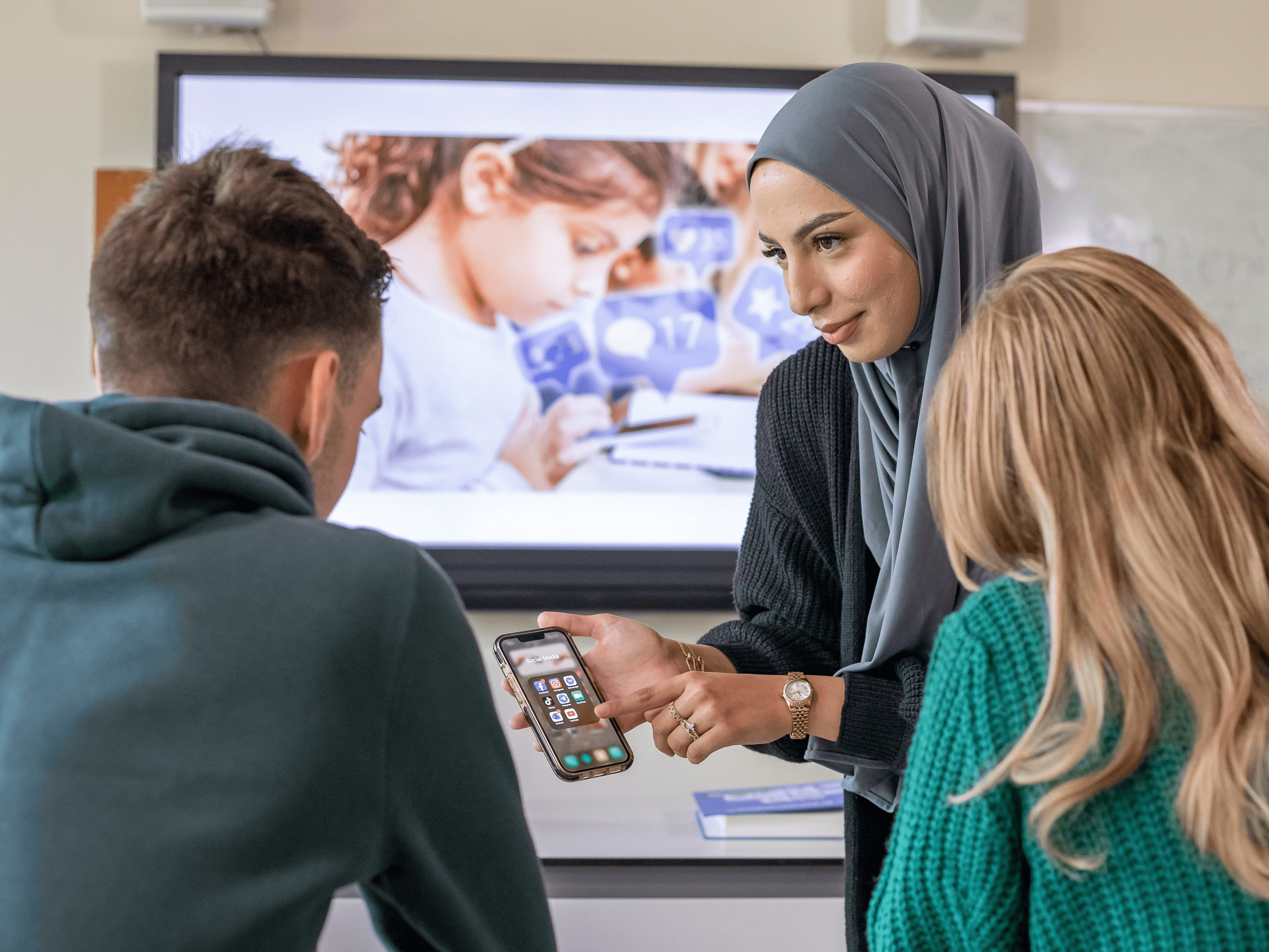Student wijst op een telefoon en staat voor 2 studenten